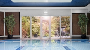 A swimming pool with a view of a garden through large glass doors. - Careys Manor & Senspa (Brockenhurst)