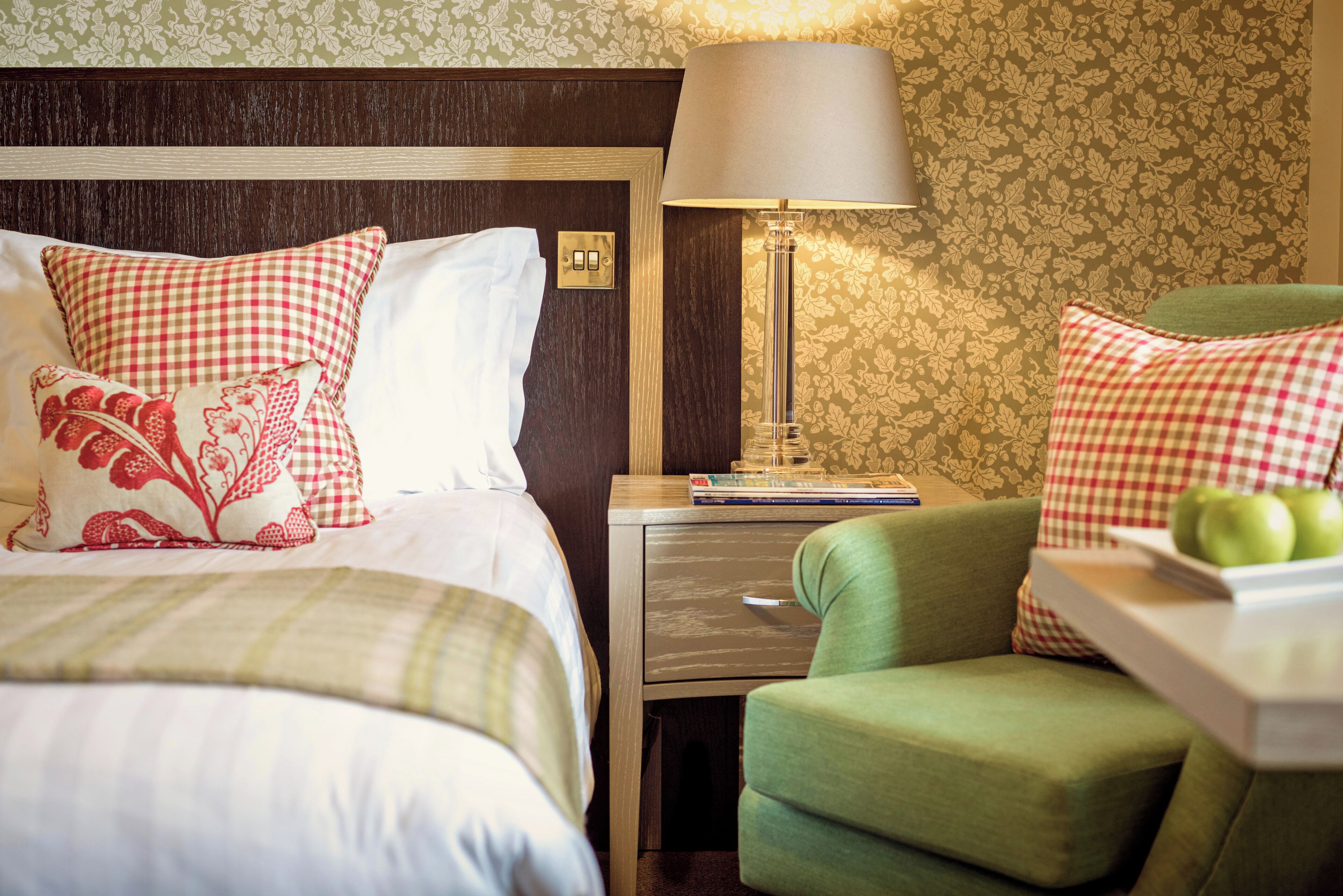Una habitación de hotel con una cama, una mesita de noche, una lámpara y un sillón verde.