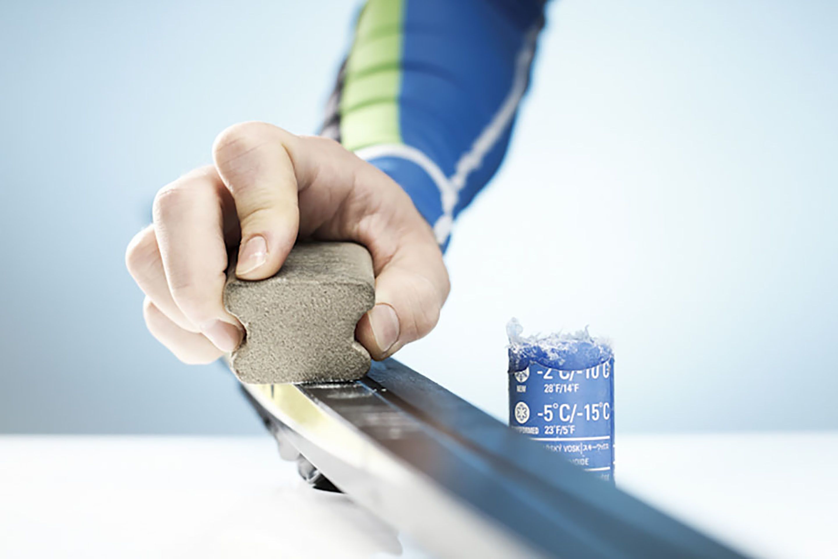 A hand holding a sanding block against a metal surface.