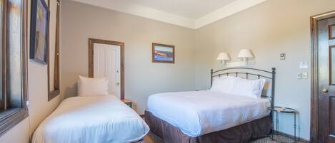 A hotel room with two beds, a ceiling fan, a small table with lamps, and a framed picture on the wall.