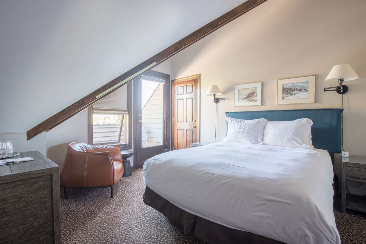Ein Hotelzimmer mit einem großen Bett, einem Holztisch, einem Ledersessel und einer Tür zu einem Außenbereich.