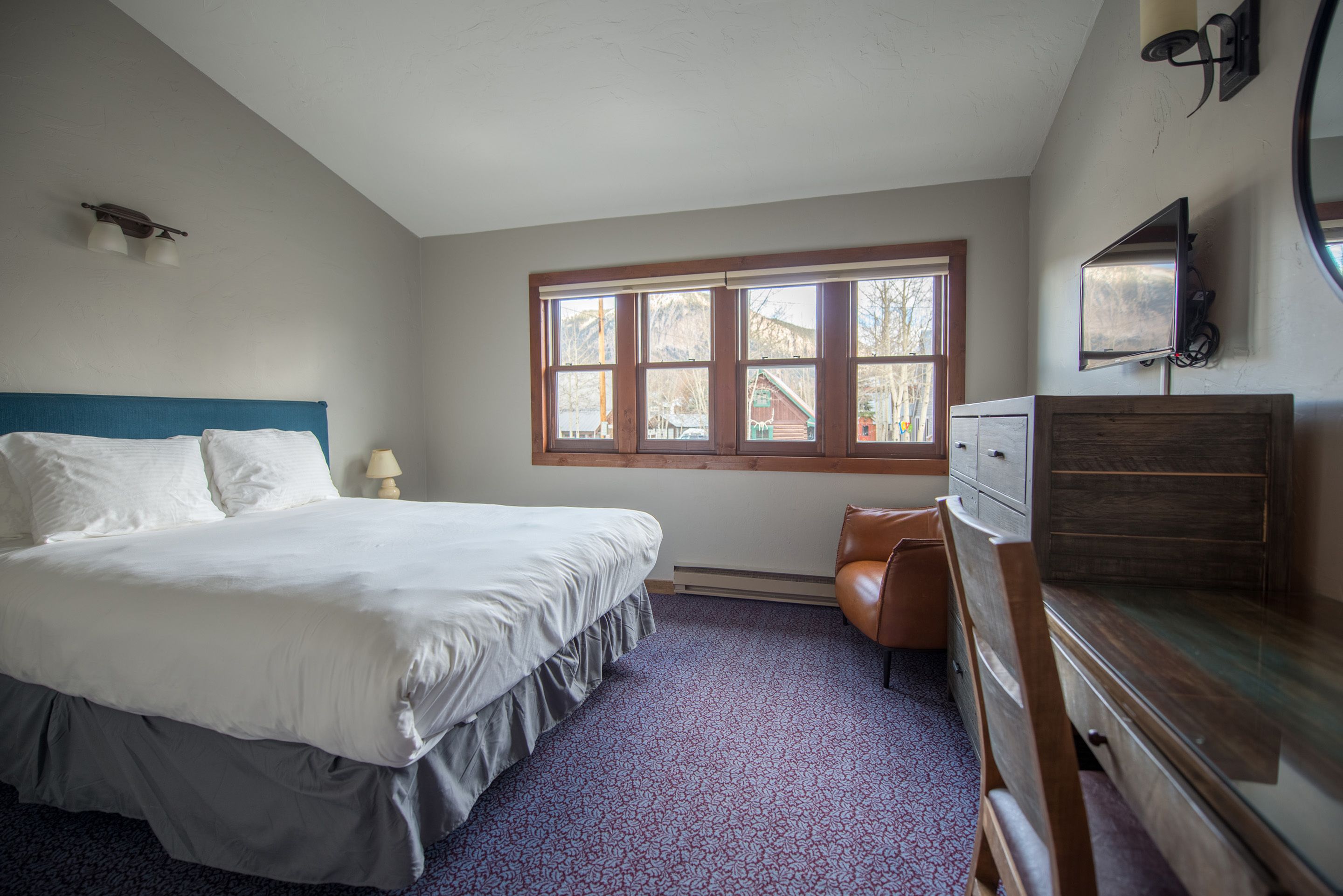 A bedroom with a large bed, a dresser, a chair, a window, and a television.