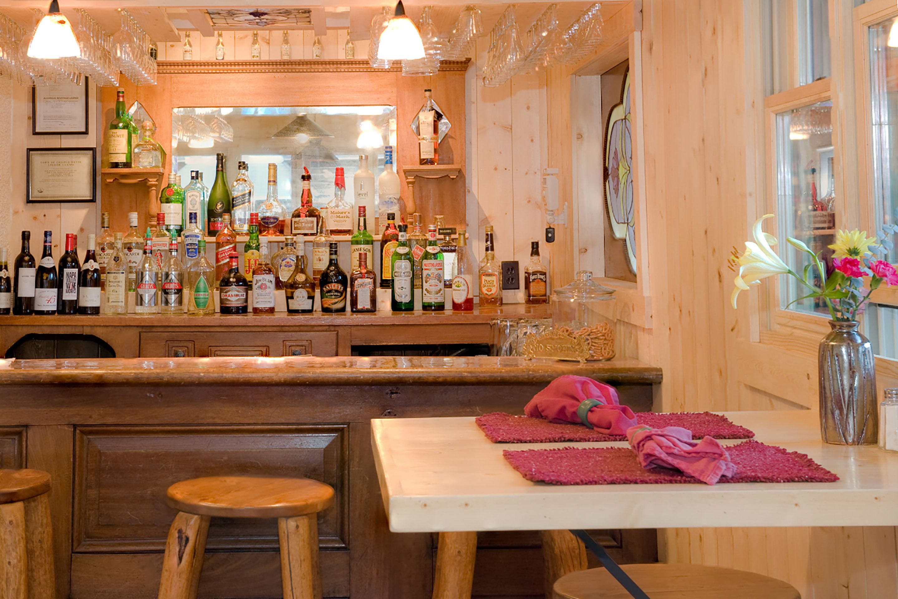 Zona de bar con decoración de madera, una variedad de botellas de licor y un florero con flores sobre una mesa.