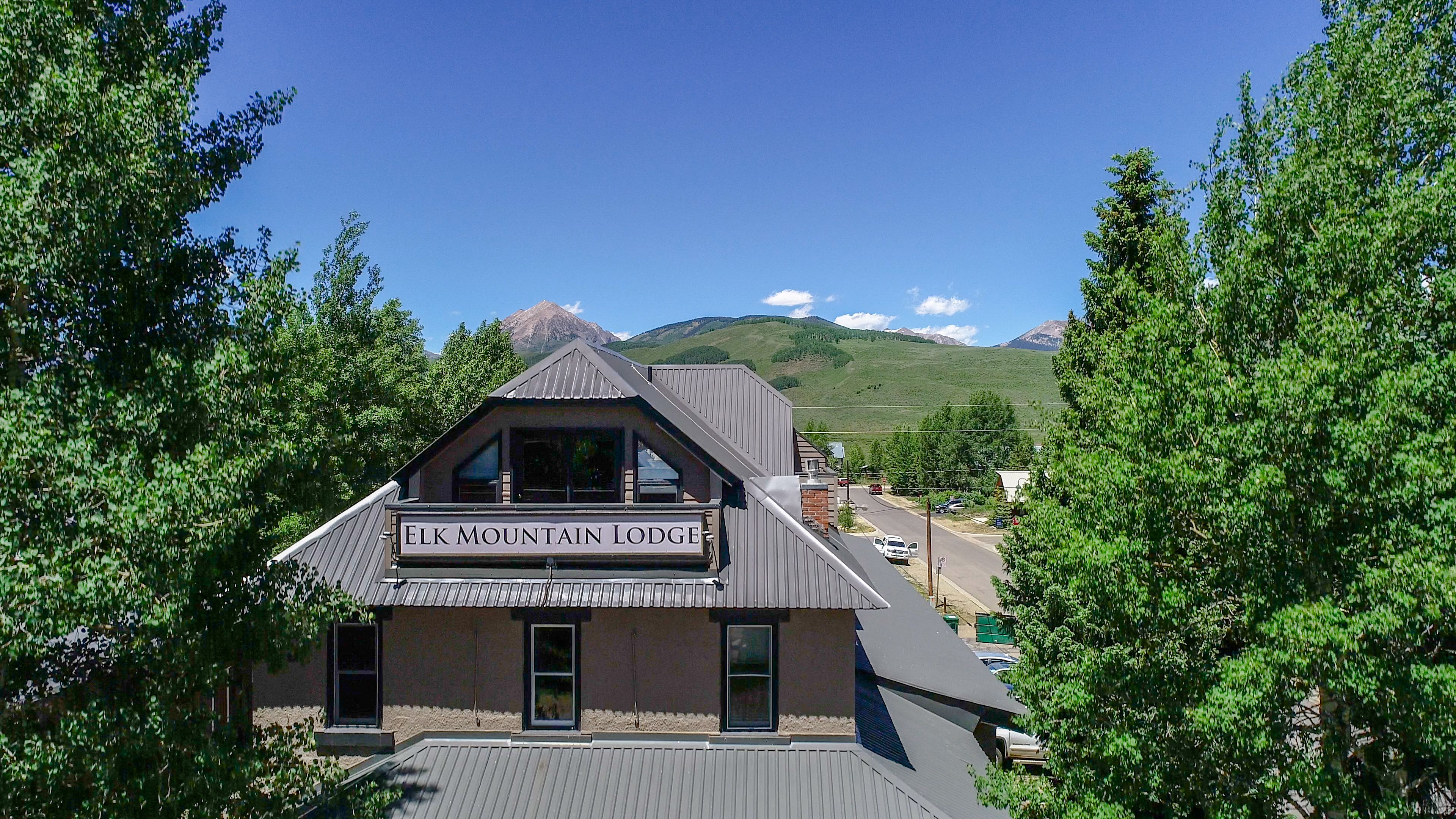 A lodge named Elk Mountain Lodge with a prominent sign, surrounded by lush greenery and a mountainous backdrop.