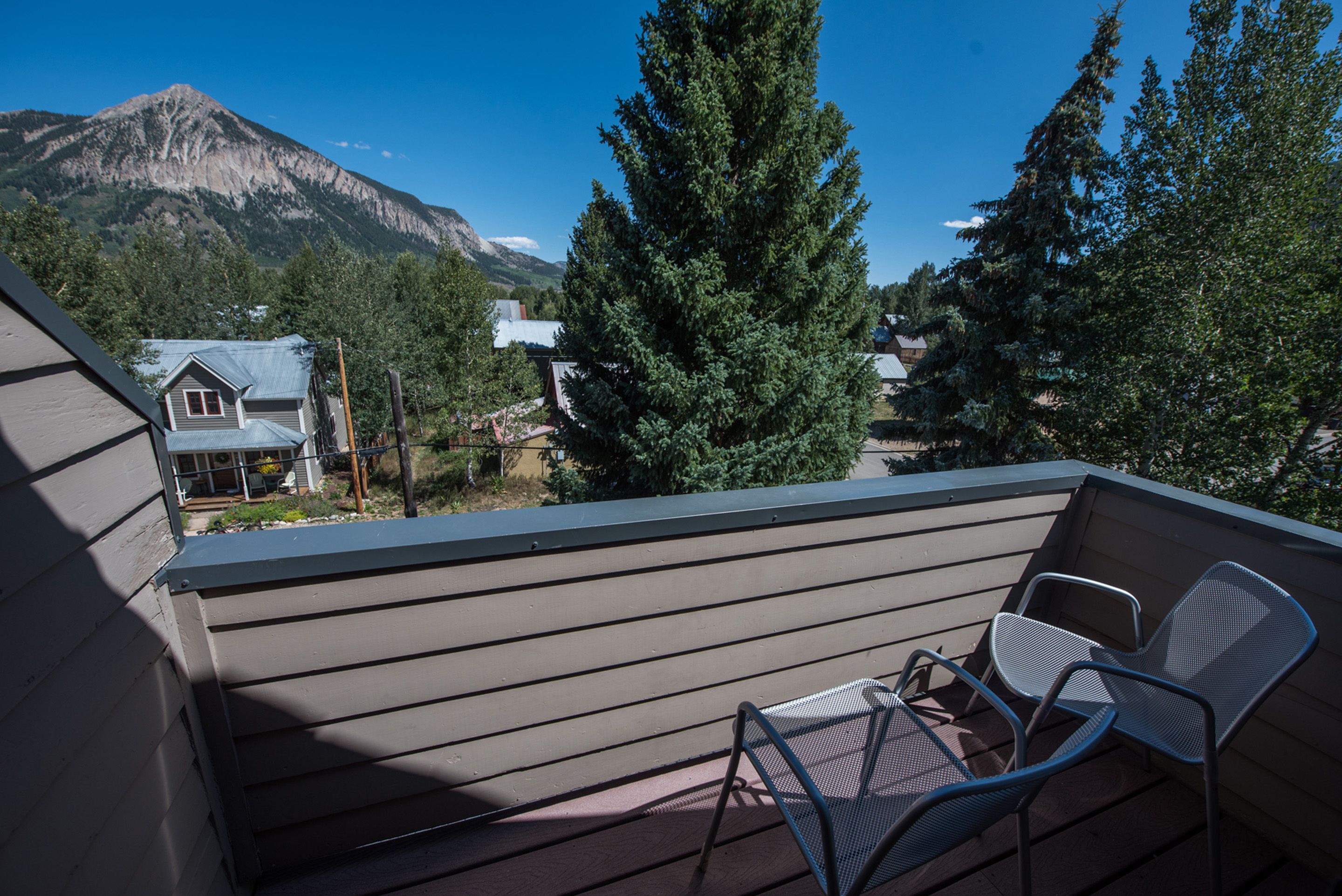 Un balcon avec vue sur une montagne, un grand arbre à feuilles persistantes et une maison en arrière-plan.