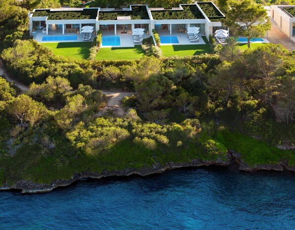 Une maison moderne avec piscine, entourée d’une végétation luxuriante et offrant une vue sur la mer.
