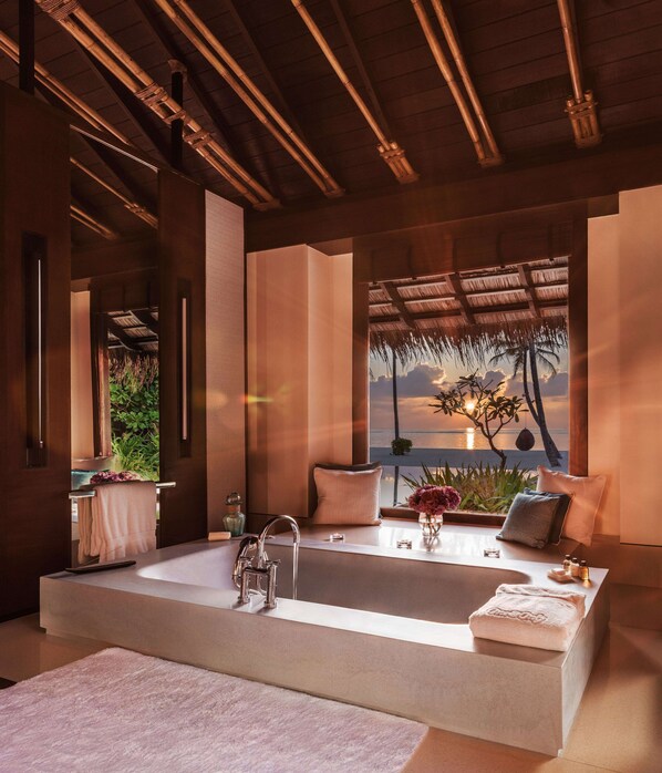 A modern bathroom with a large bathtub, a vanity with a mirror, and a view of the ocean.