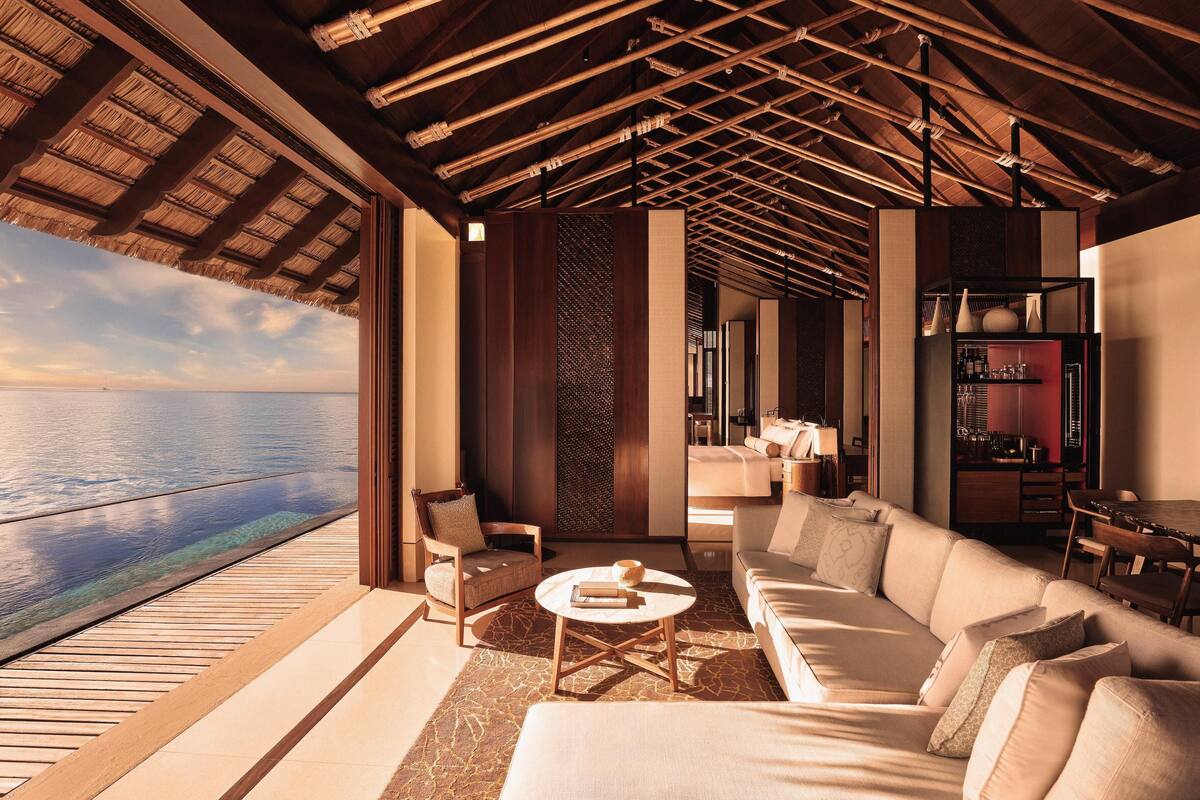 Un intérieur moderne avec une grande fenêtre donnant sur la mer, un coin salon confortable et une cuisine visible au fond.