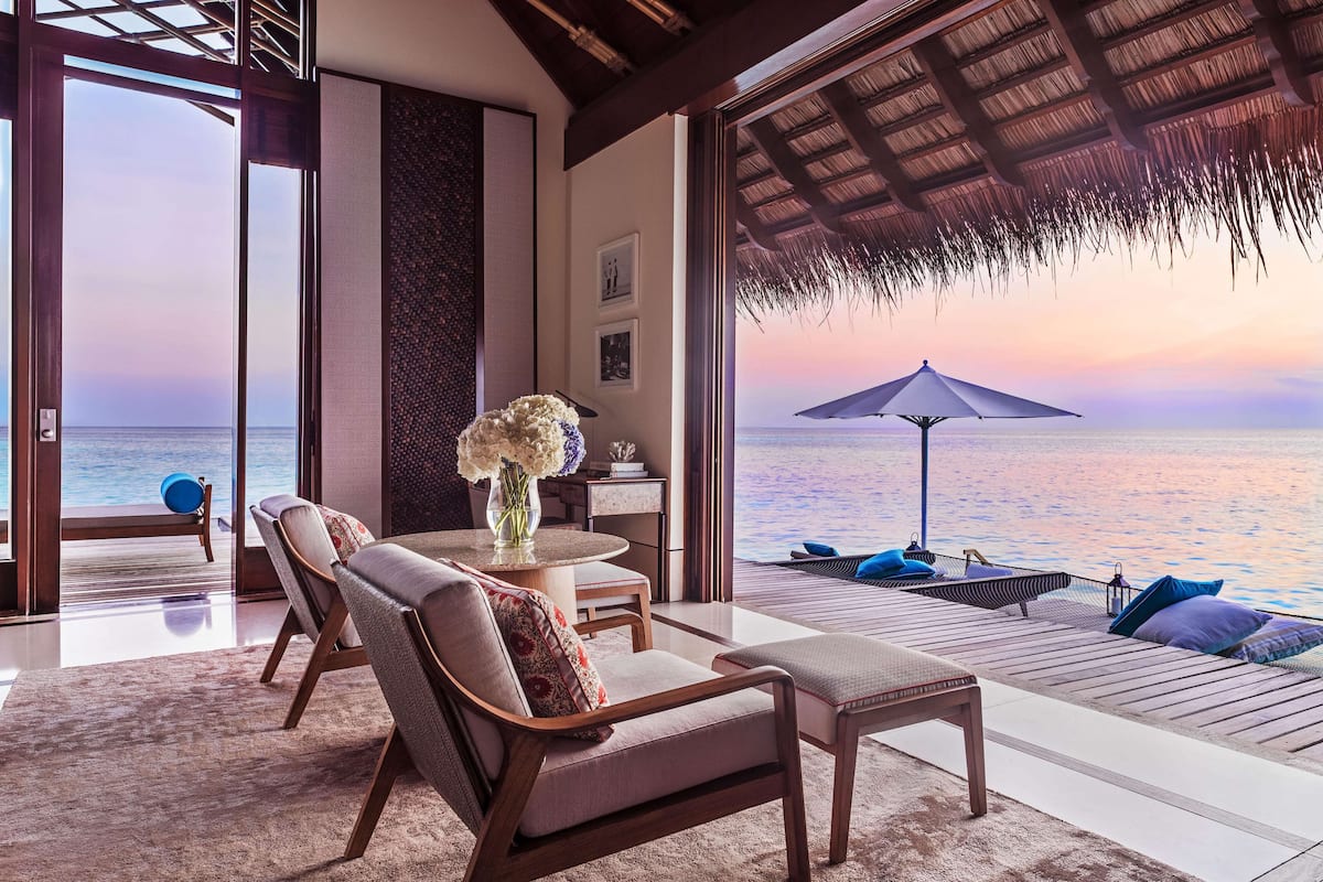 Une chambre luxueuse avec vue sur l’océan, un coin repas avec une table et des chaises, et un espace détente doté d’un toit de chaume.