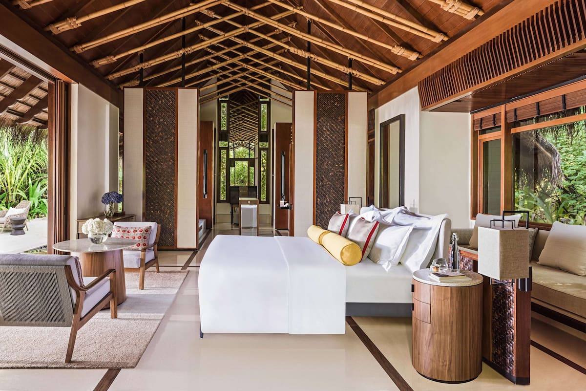 Une pièce spacieuse avec un grand lit, un canapé et une petite table. Le plafond est en bois, avec des poutres en bambou, et la pièce offre une vue sur la verdure environnante.