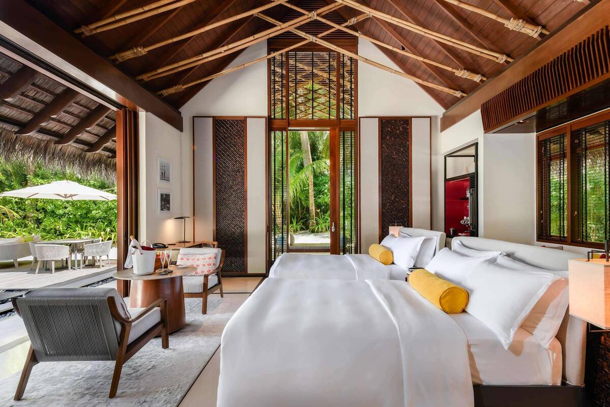 Une chambre spacieuse avec un grand lit, un coin salon avec une table et des chaises, et une vue sur une végétation luxuriante.