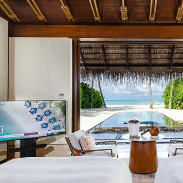 A room with a TV, a desk, two beds, and a view of the beach.