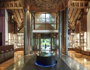 A spacious lobby with a central water feature, high ceilings with intricate woodwork, and a view of a tropical garden.