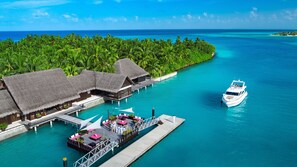 An overwater bungalows with thatched roofs, a dock, and a boat.