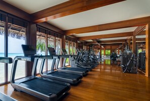 A gym with treadmills and exercise machines, large windows, and a wooden interior.