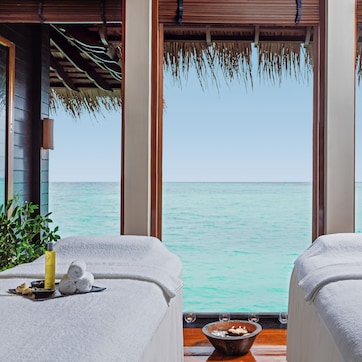 A serene spa setting with two massage tables, each with a towel, a bowl, and a bottle of SPA lotion.