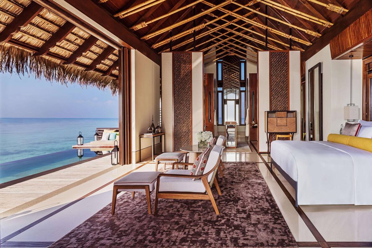 Une chambre à coucher luxueuse avec un grand lit, un coin salon avec une table et une vue sur l’océan.