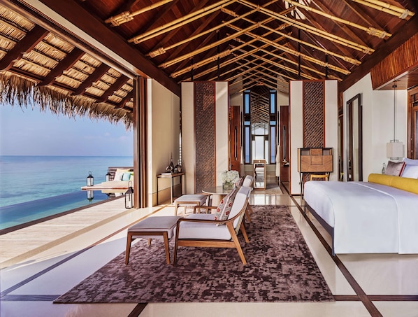 A luxurious bedroom with a large bed, a seating area with a table, and a view of the ocean.