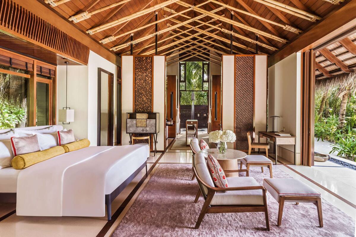 Une chambre spacieuse avec un grand lit, un bureau et une chaise, dotée d’un plafond en bois et offrant une vue sur la verdure environnante.