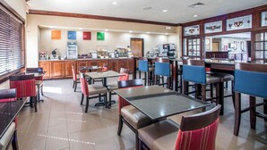 Un restaurante con varias mesas y sillas, una barra con una máquina de café y un panel con la carta.