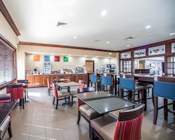Un restaurante con varias mesas y sillas, una barra con una máquina de café y un panel con la carta.