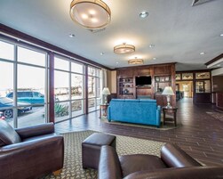 Amplia sala de estar con un sofá azul, sillones de cuero y un televisor de pantalla plana montado en un mueble de madera. Grandes ventanas ofrecen vistas a coches estacionados afuera.