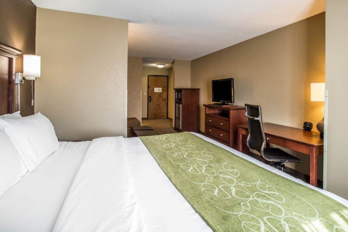 Ein Hotelzimmer mit einem Bett, einem Schreibtisch, einem Sessel, einem Fernseher und einer Tür zu einem weiteren Raum.