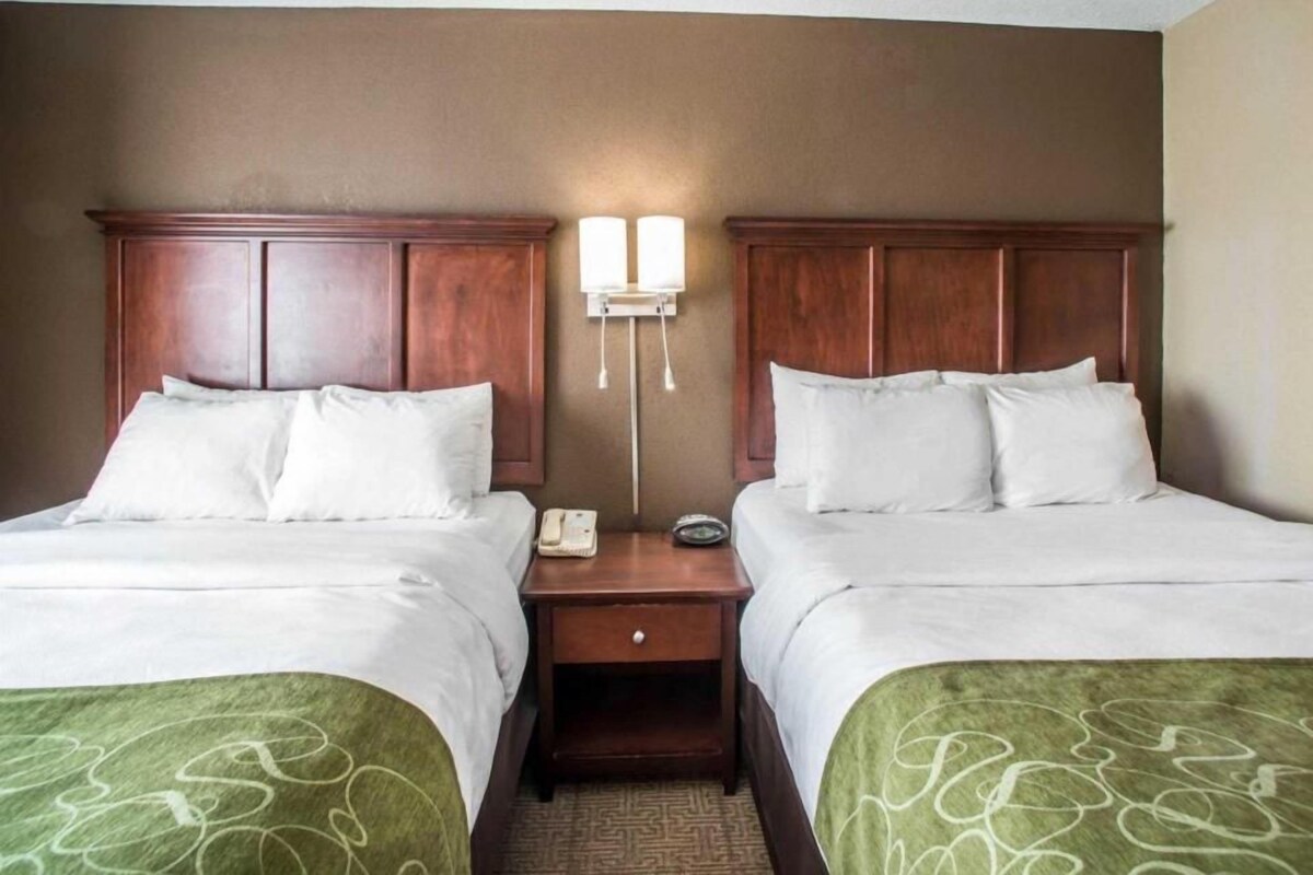 A hotel room with two beds, a nightstand, and a wall-mounted light fixture.