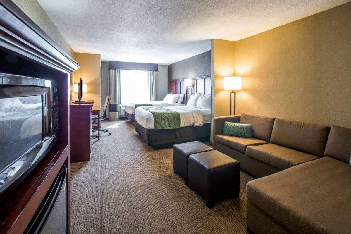 Ein Hotelzimmer mit einem großen Flachbildfernseher, zwei Betten, einem Sofa und einem Schreibtisch.