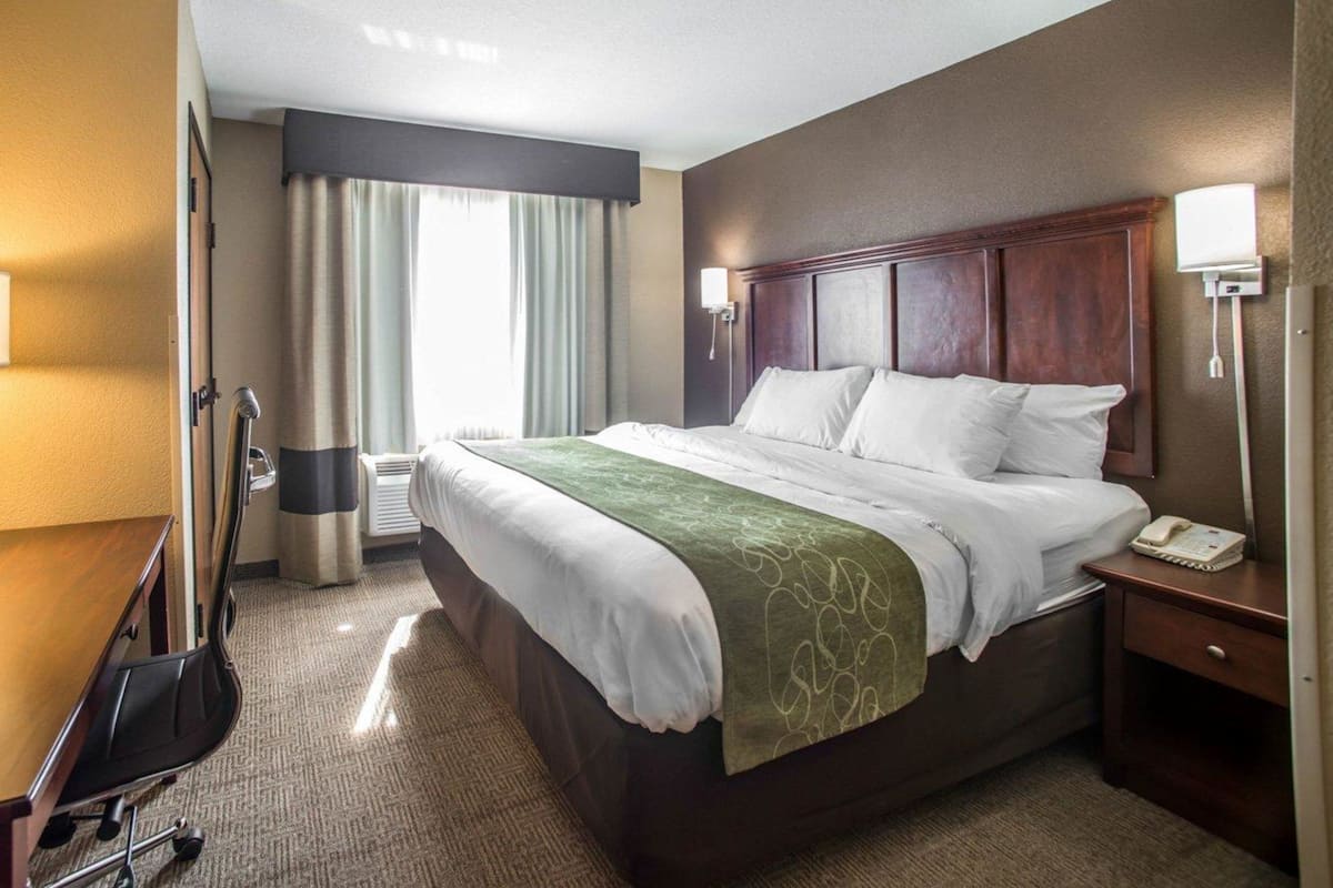 Ein Hotelzimmer mit einem großen Bett, einem Schreibtisch, einem Stuhl, einer Lampe und einem fenster mit Vorhängen.