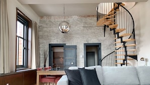 Un salon moderne avec un canapé gris, un escalier en bois et un coin repas avec des chaises rouges.