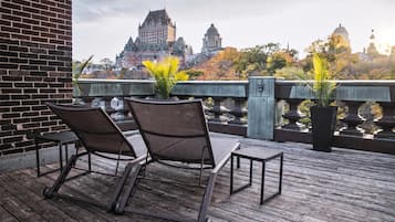 Una terraza de madera con dos sillas y plantas en macetas, con vistas a un paisaje urbano histórico con arquitectura distintiva.