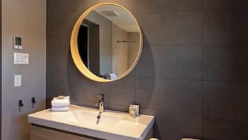 A modern bathroom with a round mirror, a white sink, and a toilet.