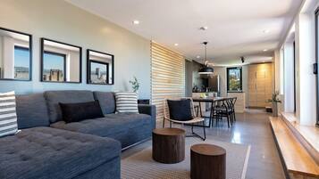 A modern living room with a grey sofa, a dining area, and a kitchen in the background.