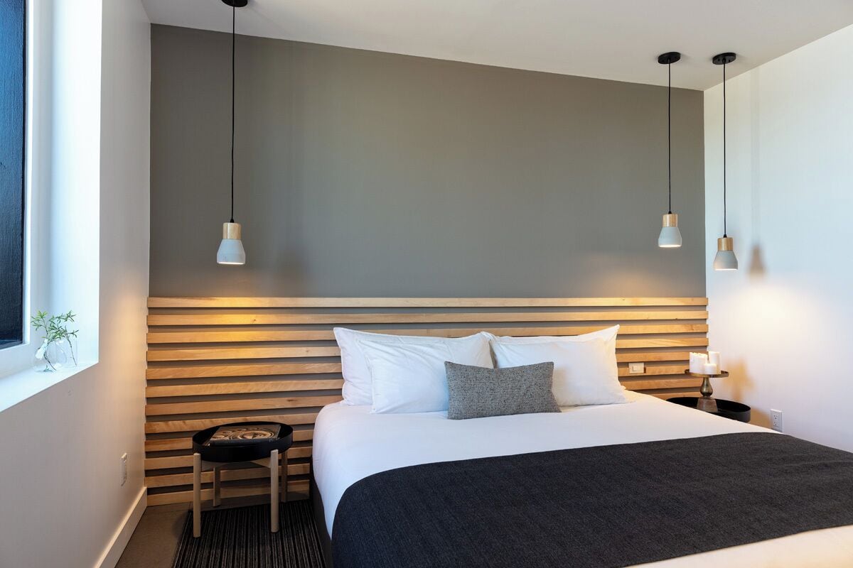 A modern hotel room with a large bed, a wooden headboard, and two pendant lights.