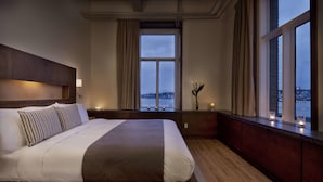 Une chambre d’hôtel avec un grand lit, une vue sur la ville grâce à de grandes fenêtres et un plancher en bois.