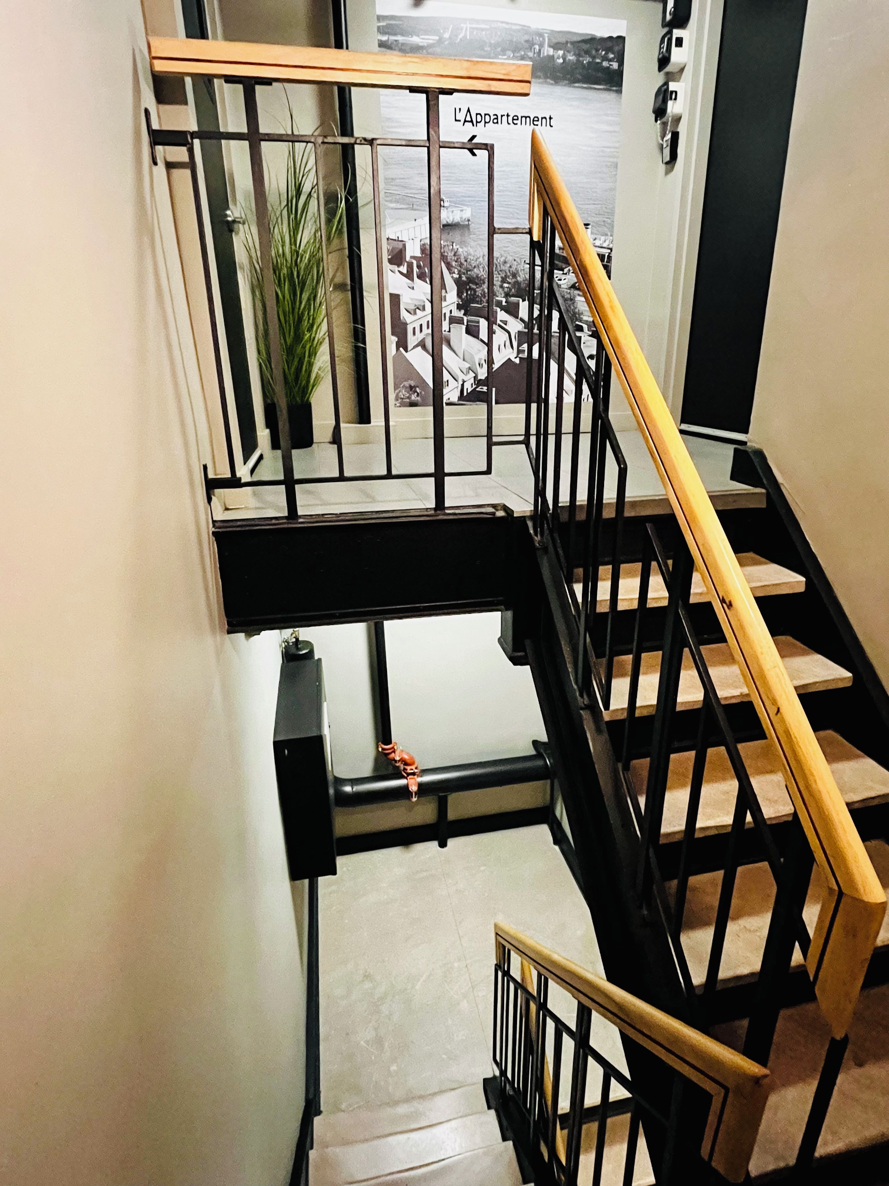 A staircase with a wooden handrail and black railings, leading to an apartment with a view of a body of water and buildings.