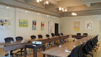 Een congreszaal met een lange tafel, meerdere stoelen, een projectiescherm en kunstwerken aan de wanden.