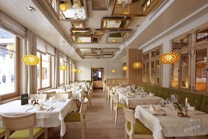 Restaurante com várias mesas preparadas para refeições, com decoração clássica, elementos em madeira e iluminação pendente.