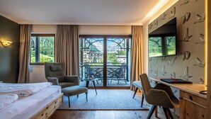 Habitación de hotel con cama, escritorio, silla y balcón con vistas a montañas y edificios.