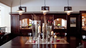 Un comedor con una mesa de madera dispuesta para cuatro personas, rodeada de sillas. Hay tres lámparas colgantes sobre la mesa.