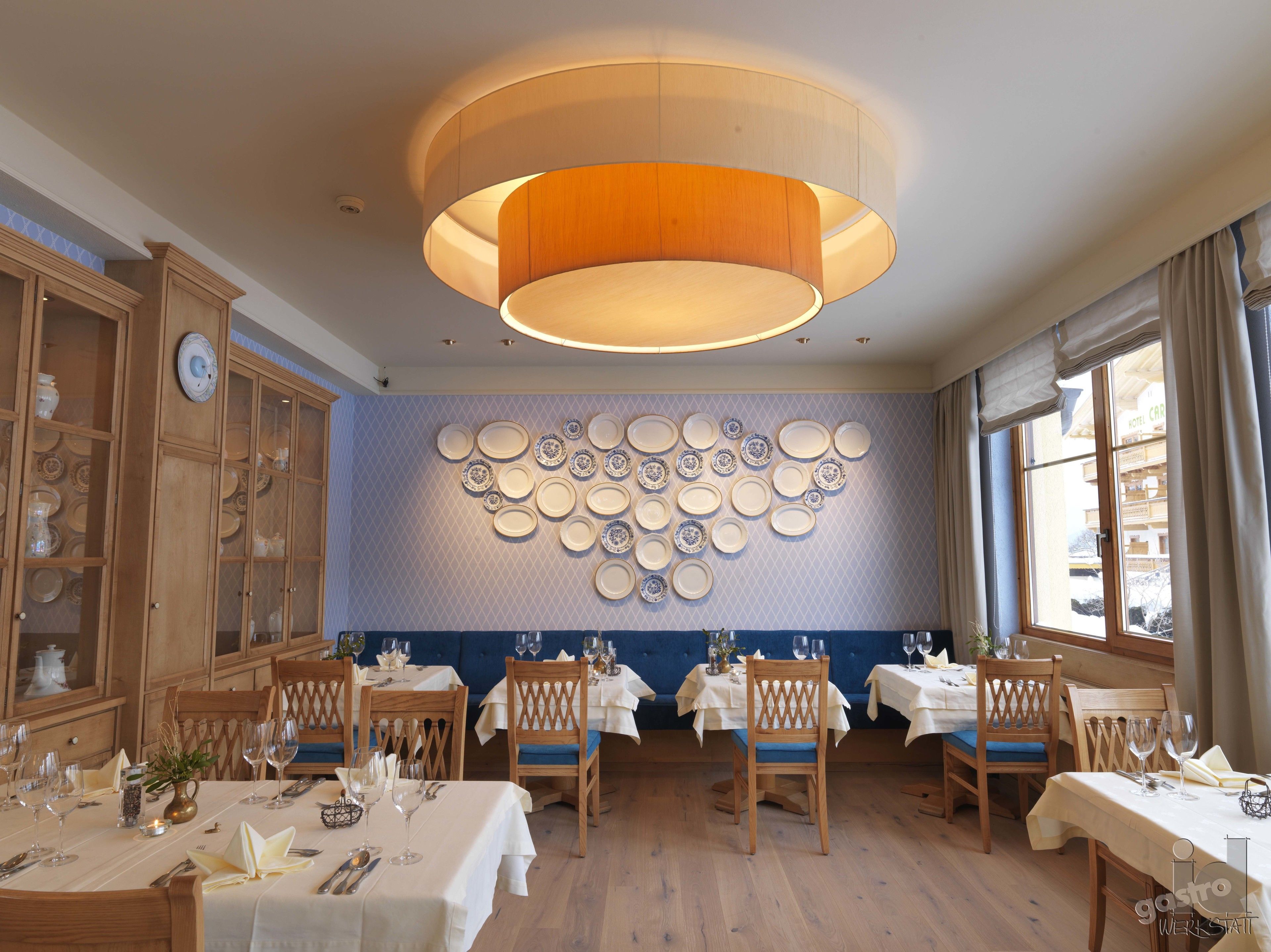 Un espace repas avec des tables dressées pour le repas, un mur décoré d’assiettes et un grand luminaire en bois.