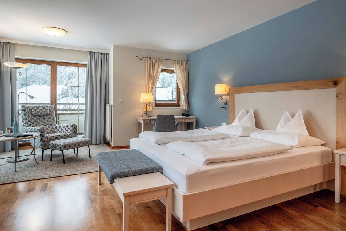 Habitación de hotel con una cama grande, dos lámparas de noche, un escritorio con una silla, una mesita y un banco.
