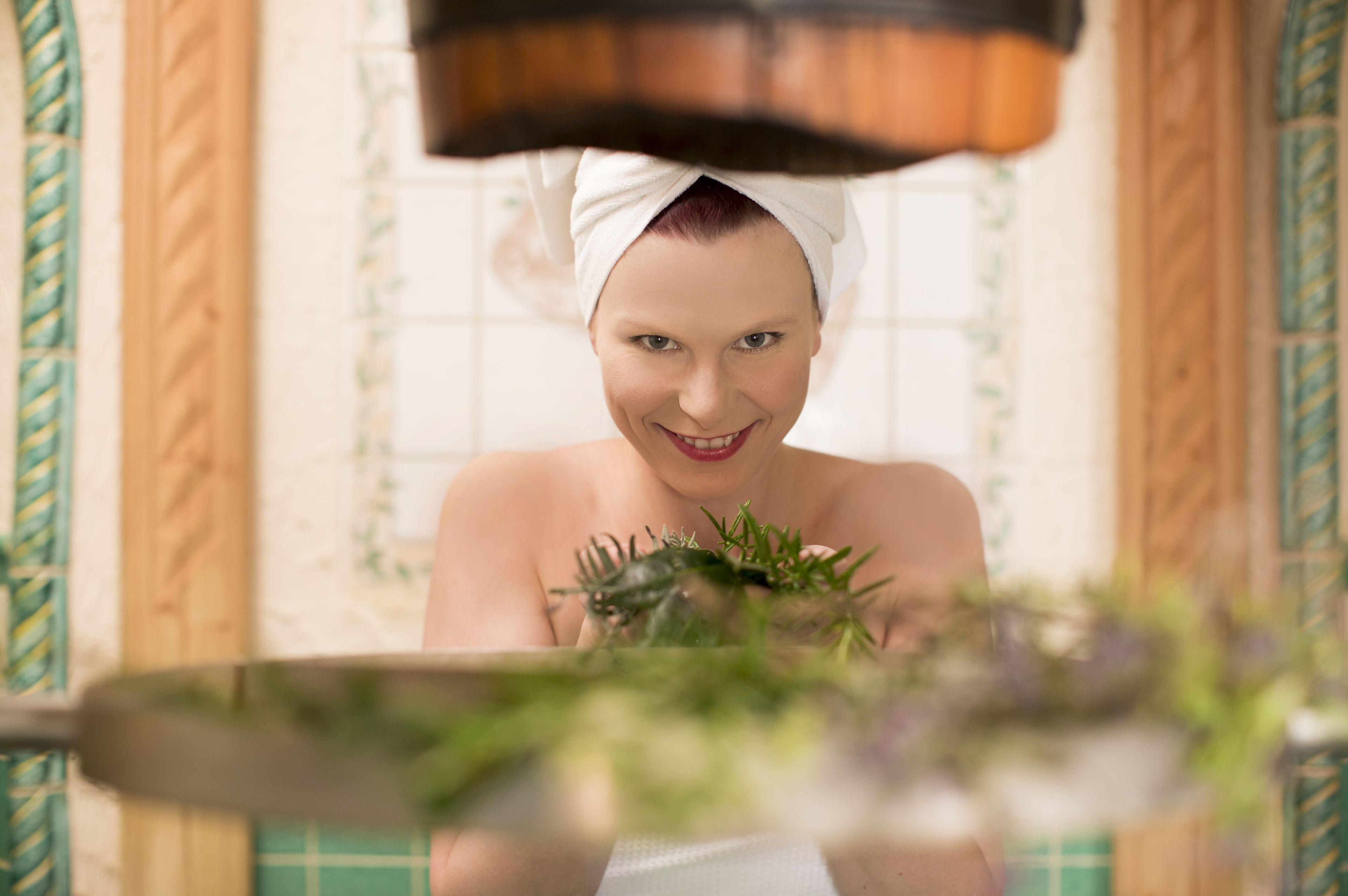 Una persona en un baño, con una toalla en la cabeza y sosteniendo una planta.