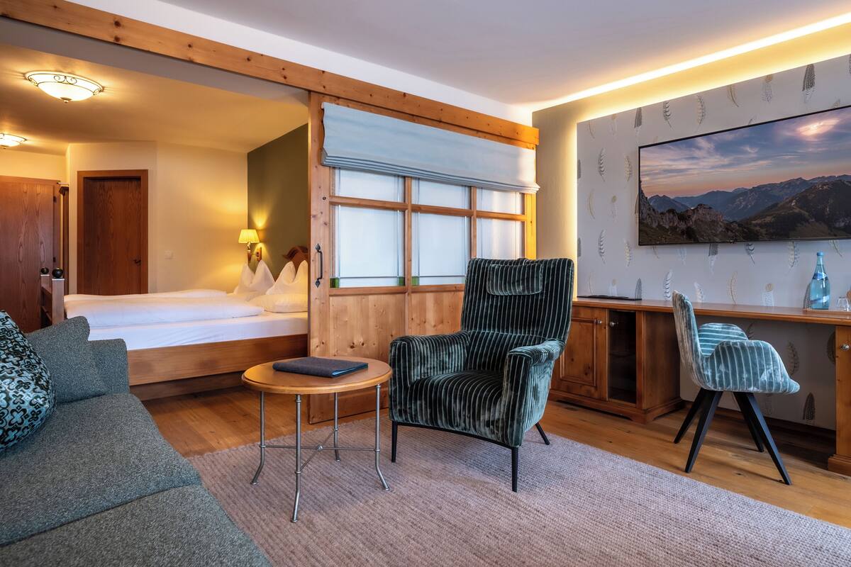 Una habitación de hotel acogedora con cama, zona de estar con sofá y sillón, una mesita y un escritorio con silla.