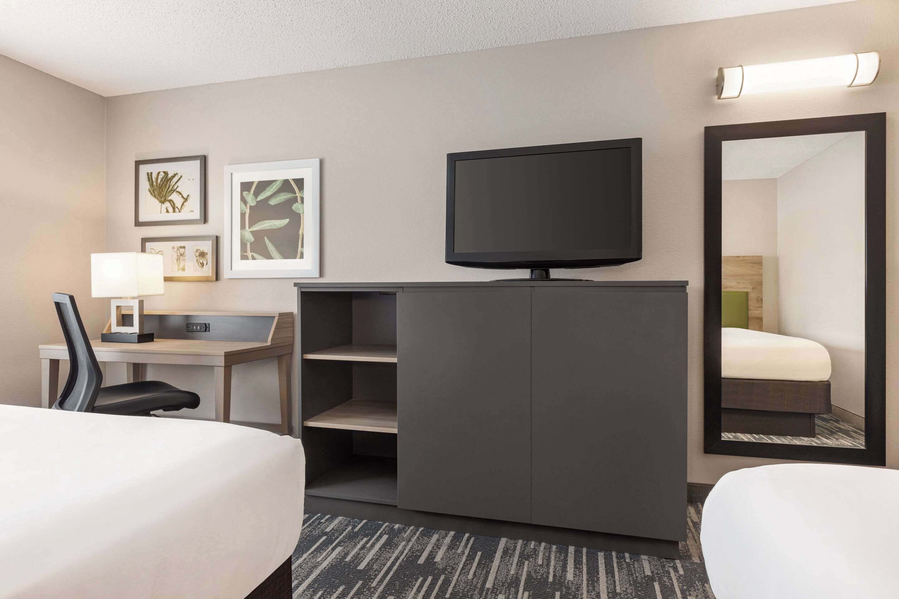 A hotel room with a bed, a desk with a chair, a television, and a mirror.