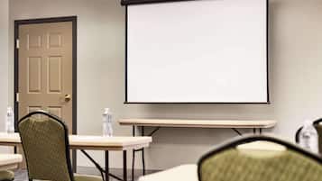 A conference room with a projector screen, a door, and two tables with chairs.