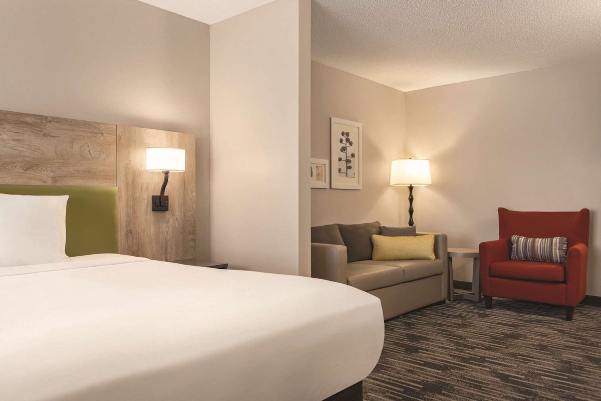 A hotel room with a large bed, a sofa, a red armchair, and two wall-mounted lamps.