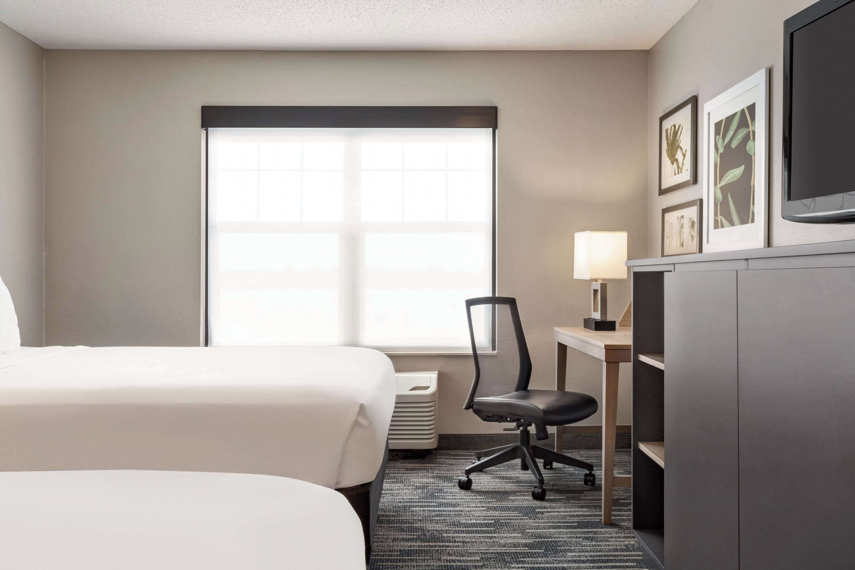 Une chambre d’hôtel avec un lit, un bureau, une chaise, une télévision et des tableaux encadrés au mur.