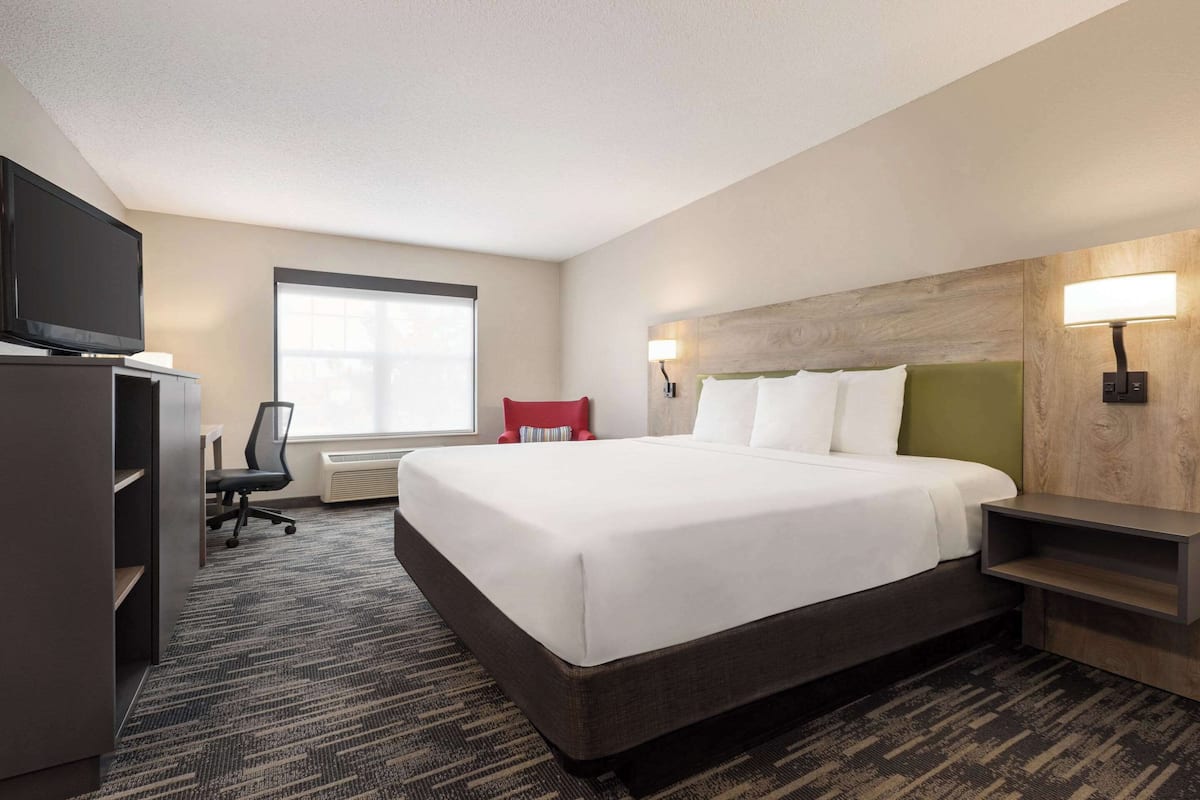 A hotel room with a large bed, a TV, a desk, and a window.
